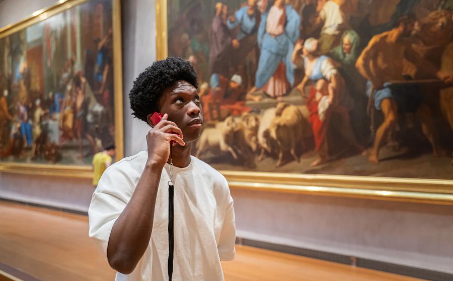 Kevin Amassouga (homme) qui pose avec un audioguide dans la salle des grands formats. 